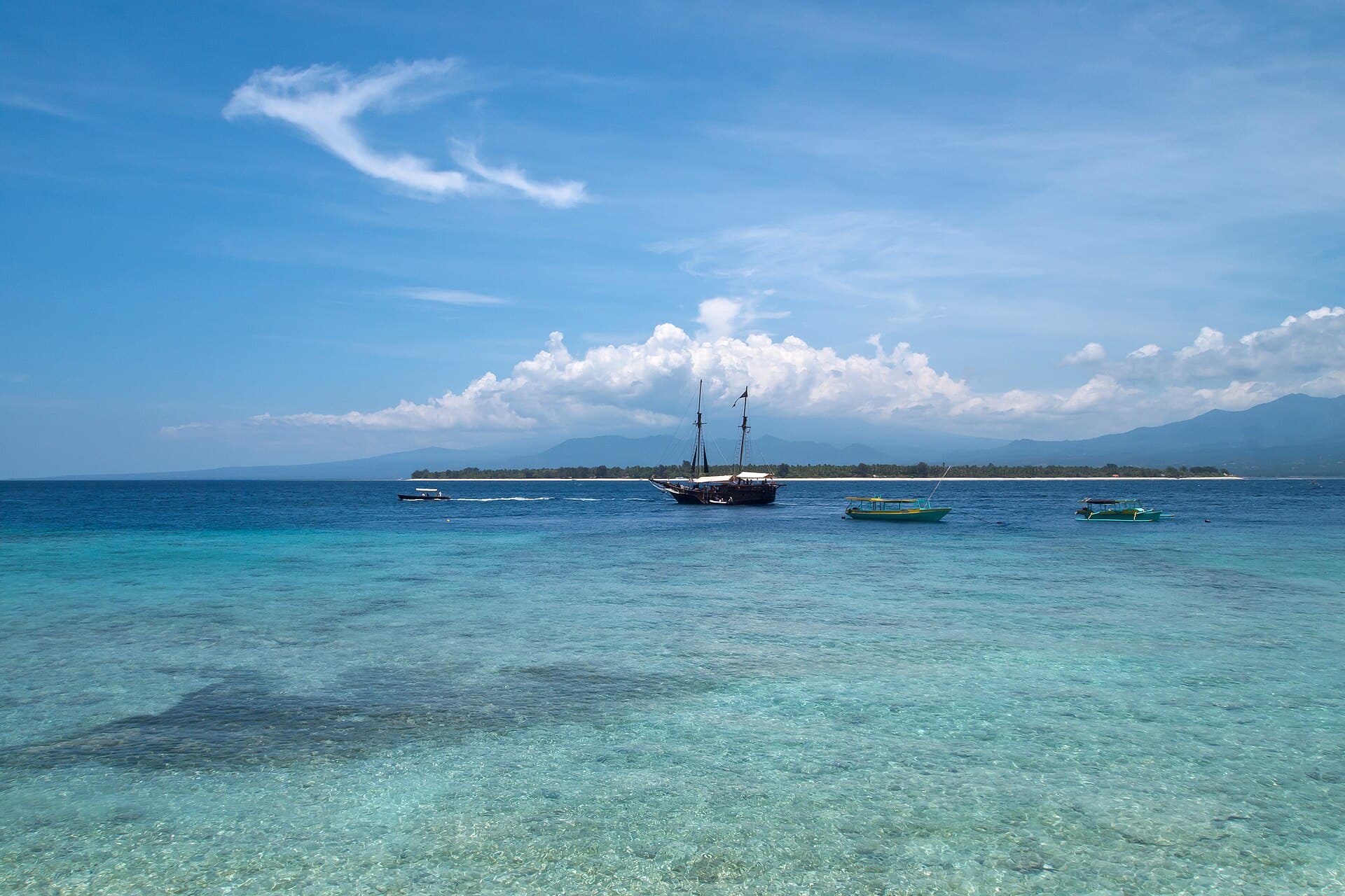 Gili Air dilihat dari Gili Meno di seberang air toska, dengan perahu layar di depannya