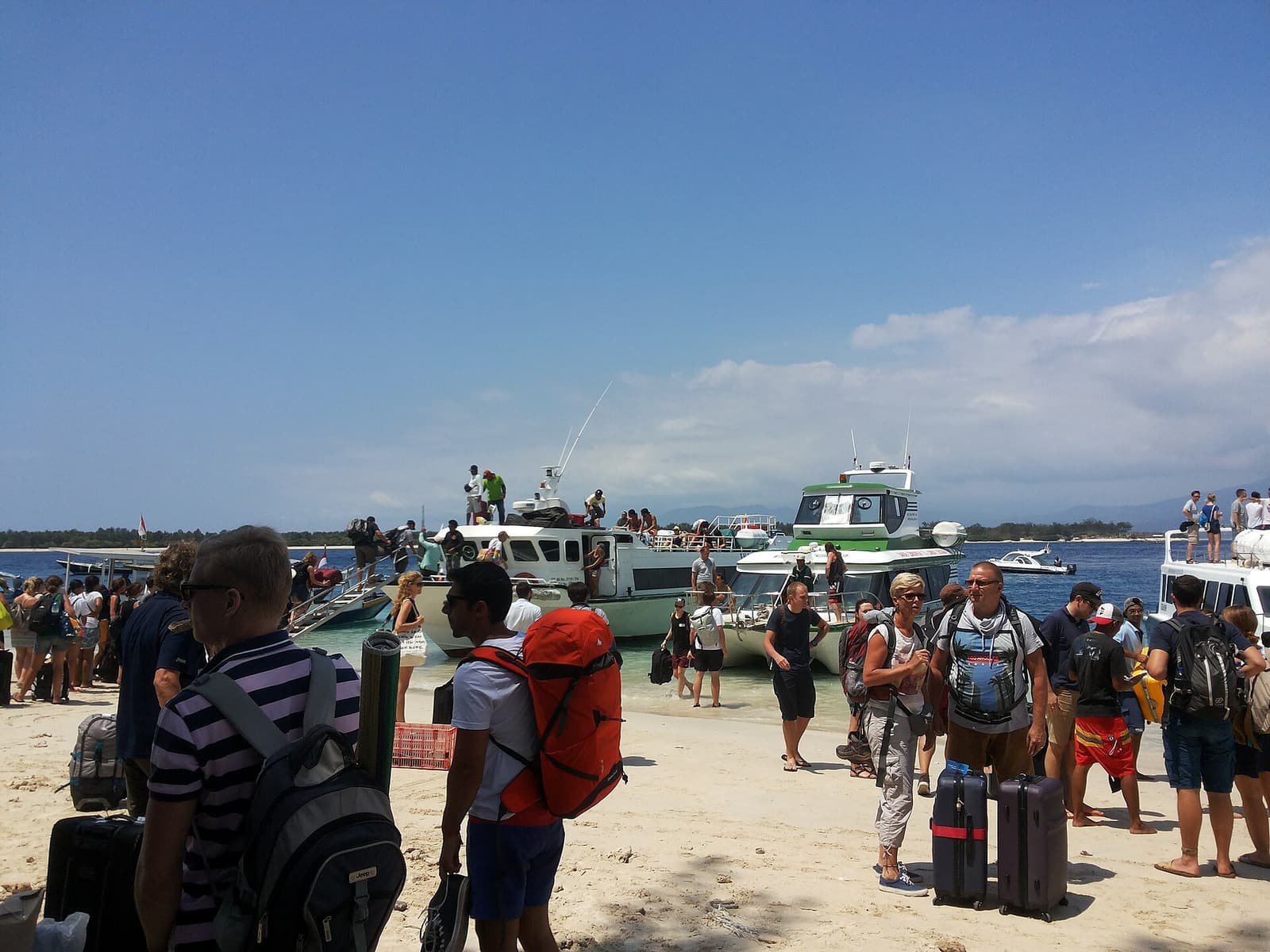 Reisende mit Gepäck warten am Strand von Gili Trawangan auf die Schnellboote
