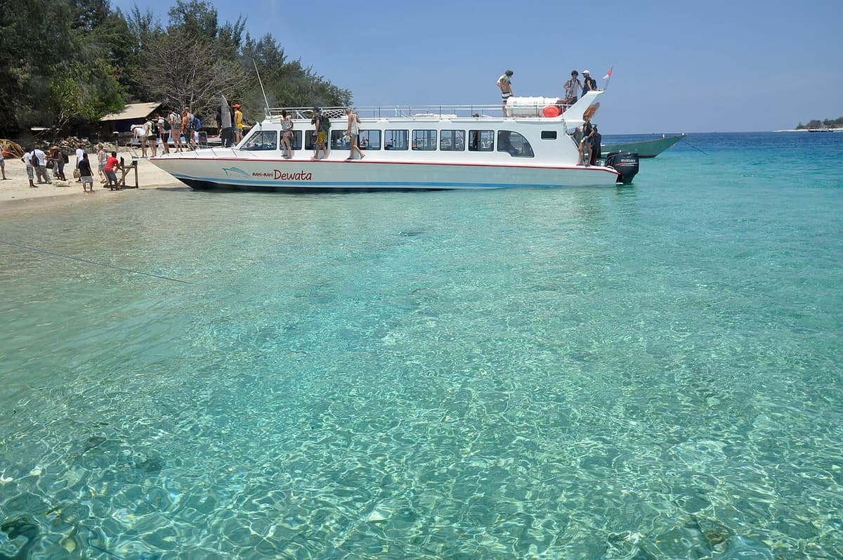 Fast boat putih bersandar di air toska di depan pantai Kepulauan Gili