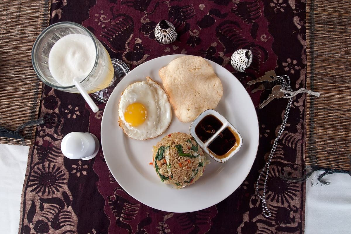 Sepiring nasi goreng dengan telur ceplok dan kerupuk di atas taplak batik