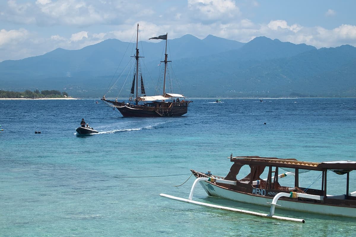 Kapal layar tradisional berlabuh di depan Gili Meno dengan pegunungan Lombok di belakangnya